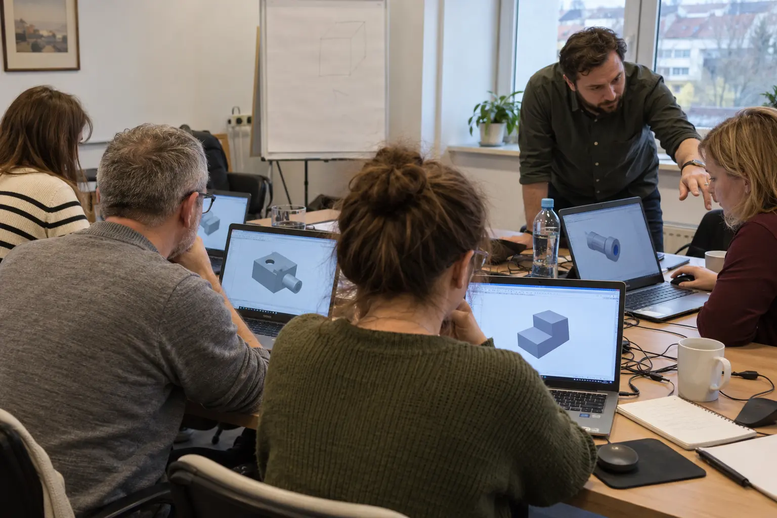 Uczestnicy szkolenia projektują modele 3D na laptopach, trener tłumaczy przy jednym ze stanowisk