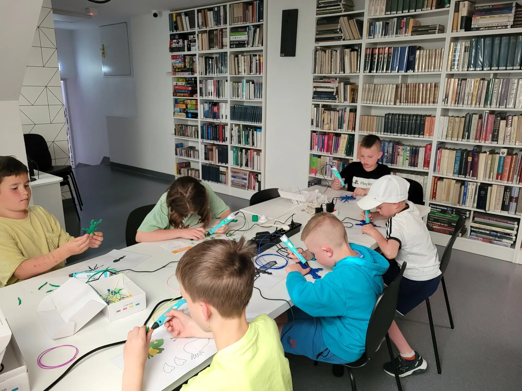 Chłopcy rysują długopisami 3D przy stole w bibliotece