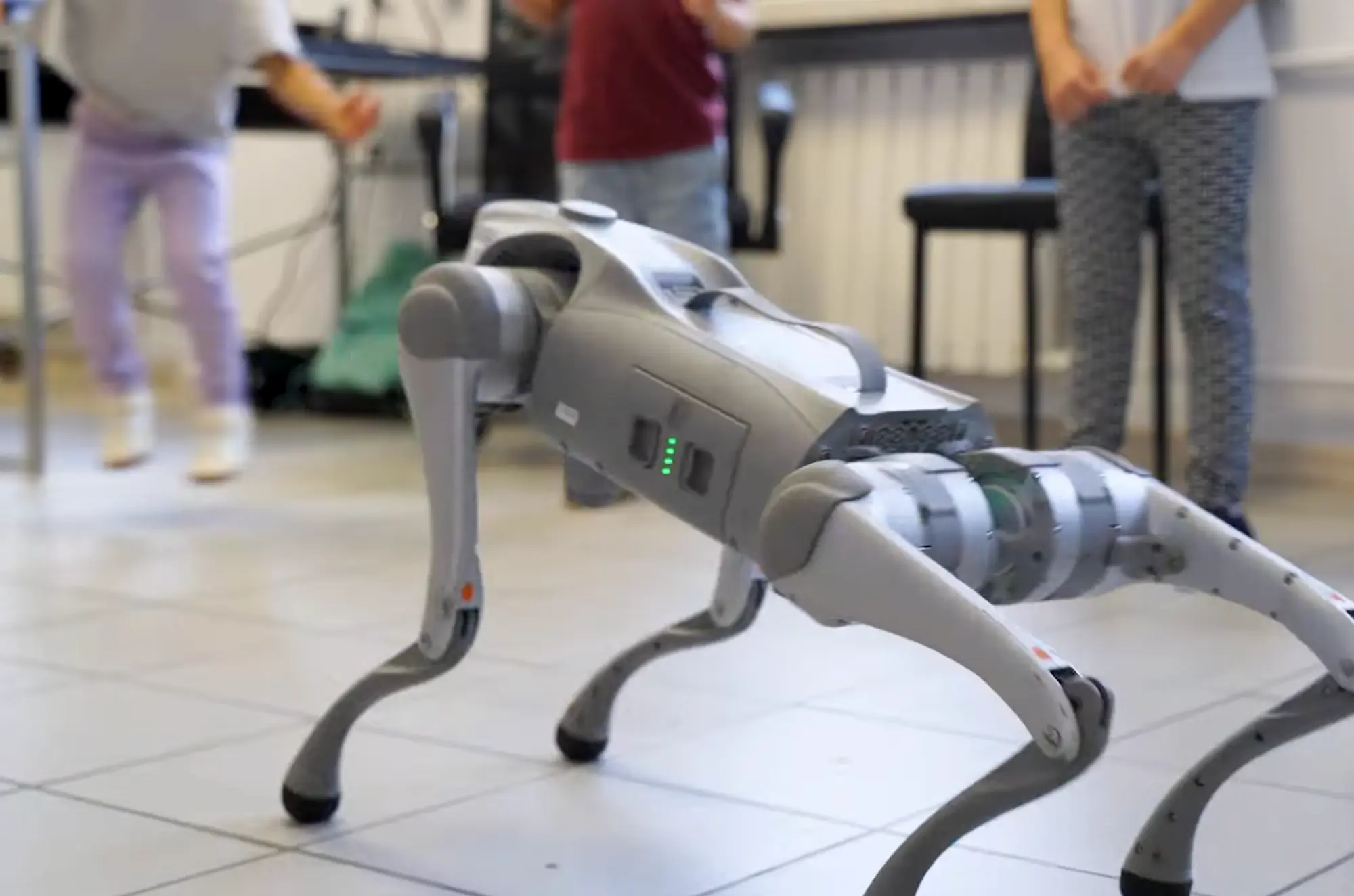 Robot w kształcie psa na podłodze, w tle dzieci