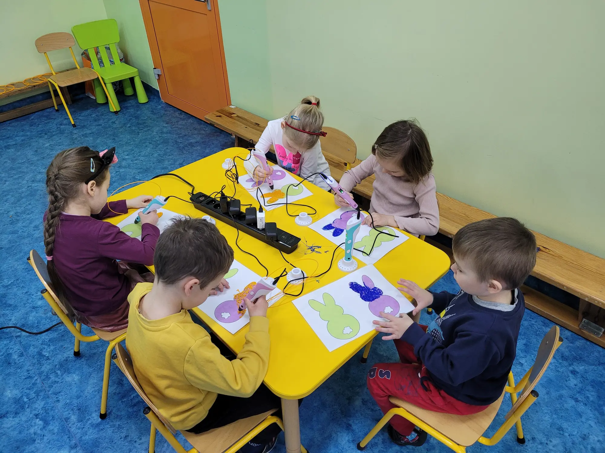 Dzieci rysują długopisami 3D przy żółtym stole